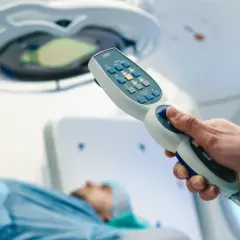 Dłoń trzymająca kontroler aparatu do radioterapii, pacjent na stole. Nowoczesna chemia biologiczna na raka.