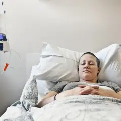 Kobieta zmagająca się z rakiem piersi z przerzutami odpoczywa w szpitalnym łóżku, podłączona do pompy infuzyjnej.