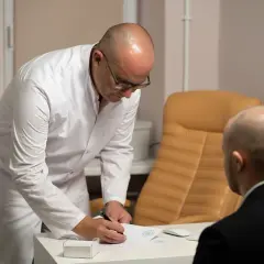 Lekarz w białym kitlu pochyla się nad dokumentami, omawiając z pacjentem wyniki badań, które mogą wskazywać na raka in situ sutka.