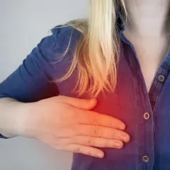 Kobieta z blond włosami dotyka piersi, gdzie widoczny jest czerwony obszar bólu, sugerujący potrzebę biopsji torbieli w piersiach.