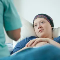 Młoda pacjentka w chustce na głowie leży w łóżku, słuchając pielęgniarki. To może być początek walki z chorobą, gdzie rak przedinwazyjny co to znaczy, jest kluczowym pytaniem.