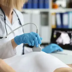 Lekarka wykonuje badanie USG piersi, sprawdzając znamiona. Na ekranie komputera widoczny obraz.