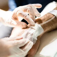 Ręce w rękawiczkach zakładają opatrunek na wenflon. Pacjent przechodzi chemioterapię, która bywa trudna, ale każdy cykl przybliża do zdrowia.