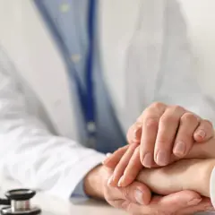 Lekarz uspokaja pacjenta, który martwi się o objawy raka. Na stole leży stetoskop.