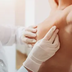 Lekarz w białej rękawiczce delikatnie bada pierś, lokalizując znacznik tytanowy po biopsji.