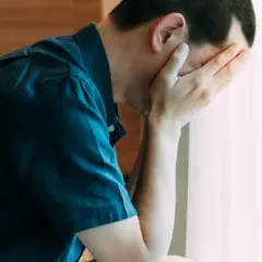 Mężczyzna z rękami na twarzy, zmartwiony. Warto znać objawy raka jądra.