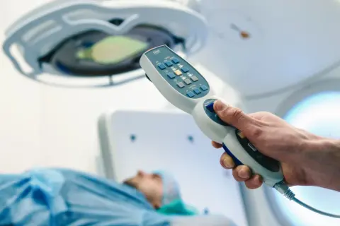 Dłoń trzymająca kontroler aparatu do radioterapii, pacjent na stole. Nowoczesna chemia biologiczna na raka.