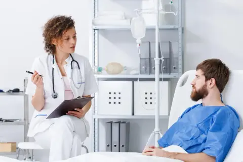 Lekarka omawia z pacjentem potencjalne immunoterapia skutki uboczne. Pacjent leży w łóżku szpitalnym, podłączony do kroplówki.