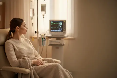 Kobieta w fotelu czeka na zakończenie terapii. Zastanawia się, ile trwa chemioterapia, podczas gdy kroplówka powoli się wchłania.