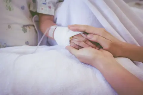 Dłoń rodzica obejmuje dłoń dziecka z wenflonem, symbol wsparcia podczas chemioterapii indukcyjnej.