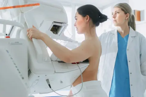 Kobieta podczas mammografii, gdzie zacienienie w mammografii co oznacza jest kluczowe dla diagnozy. Lekarka nadzoruje badanie.
