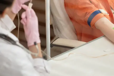 Pierwsza chemioterapia: pielęgniarka w różowych rękawiczkach przygotowuje kroplówkę dla pacjenta.
