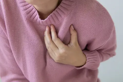 Kobieta trzyma się za klatkę piersiową, odczuwając ból lub zgrubienie pod lewą piersią.