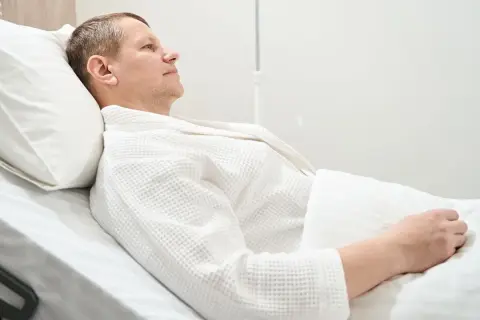 Mężczyzna w białym szlafroku leży w łóżku szpitalnym, przygotowując się do usunięcia pęcherza moczowego.