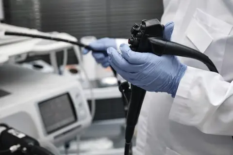 Lekarz w niebieskich rękawiczkach trzyma endoskop. Obok aparatury medycznej, która może wskazywać na zły wynik gastroskopii.