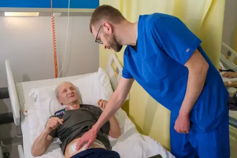 Lekarz pochyla się nad pacjentem w łóżku szpitalnym, omawiając jego rokowania po usunięciu trzustki.