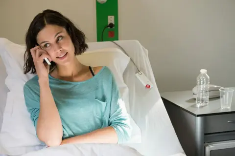Kobieta w szpitalnym łóżku rozmawia przez telefon, szukając informacji, co niszczy raka.