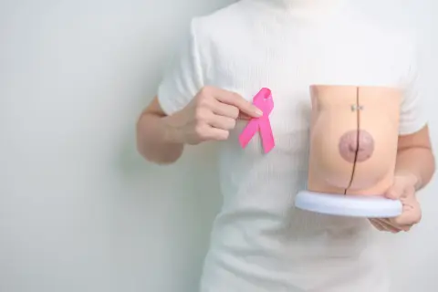 Dłoń trzyma różową wstążkę obok modelu piersi, symbolizując nadzieję po mastektomii z rekonstrukcją.