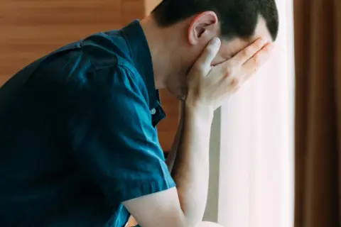 Mężczyzna z rękami na twarzy, zmartwiony. Warto znać objawy raka jądra.